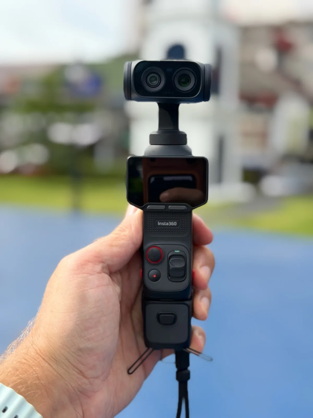 Hand hält die Insta360 Luna Ultra mit eingeschaltetem Display, grüner Hintergrund