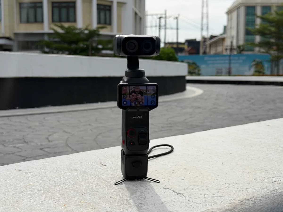 Insta360 Luna Ultra auf einem Mini-Stativ auf einer Mauer, im Hintergrund Wohngebäude und blauer Himmel